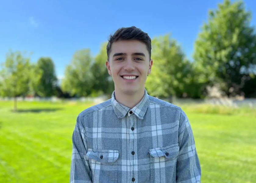 A young man standing in front of some trees.