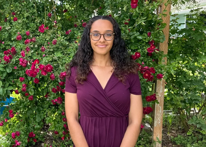 A woman in purple dress standing next to flowers.